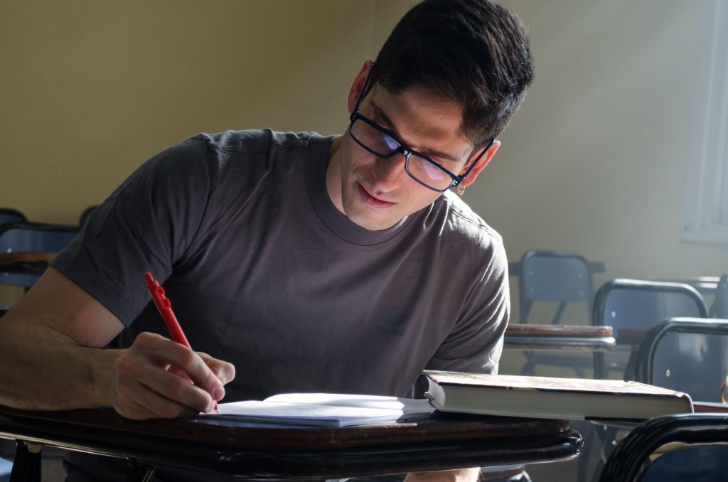 Focused student studying at a desk in a classroom with natural light streaming in.