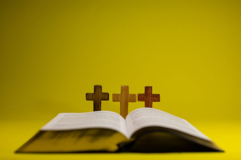 Open Bible with three wooden crosses symbolizing Christianity on a bright yellow background.